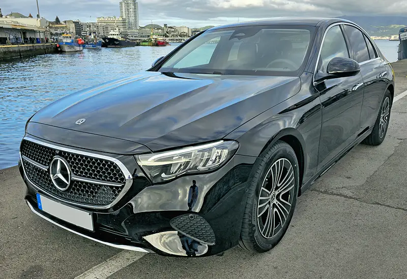 Black Mercedes-Benz executive car parked near a waterfront with a sleek design and alloy wheels. Aluguer de Frota.