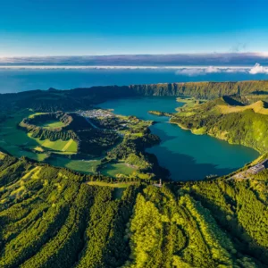 Aerial view of a lush green landscape in the Azores featuring lakes and hills under a clear blue sky.