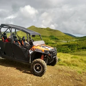 Black and orange off-road buggy parked on a dirt path with green hills in the background.
