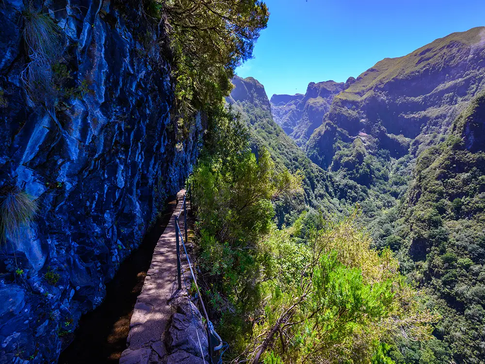 Scenic view of the Caldeirão Verde Levada trail surrounded by lush greenery and steep cliffs.