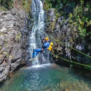 Two individuals participating in a canyoning activity near a waterfall in Madeira.