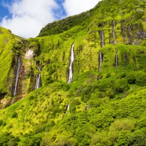 A green mountain landscape featuring multiple waterfalls cascading down the rocky surface.