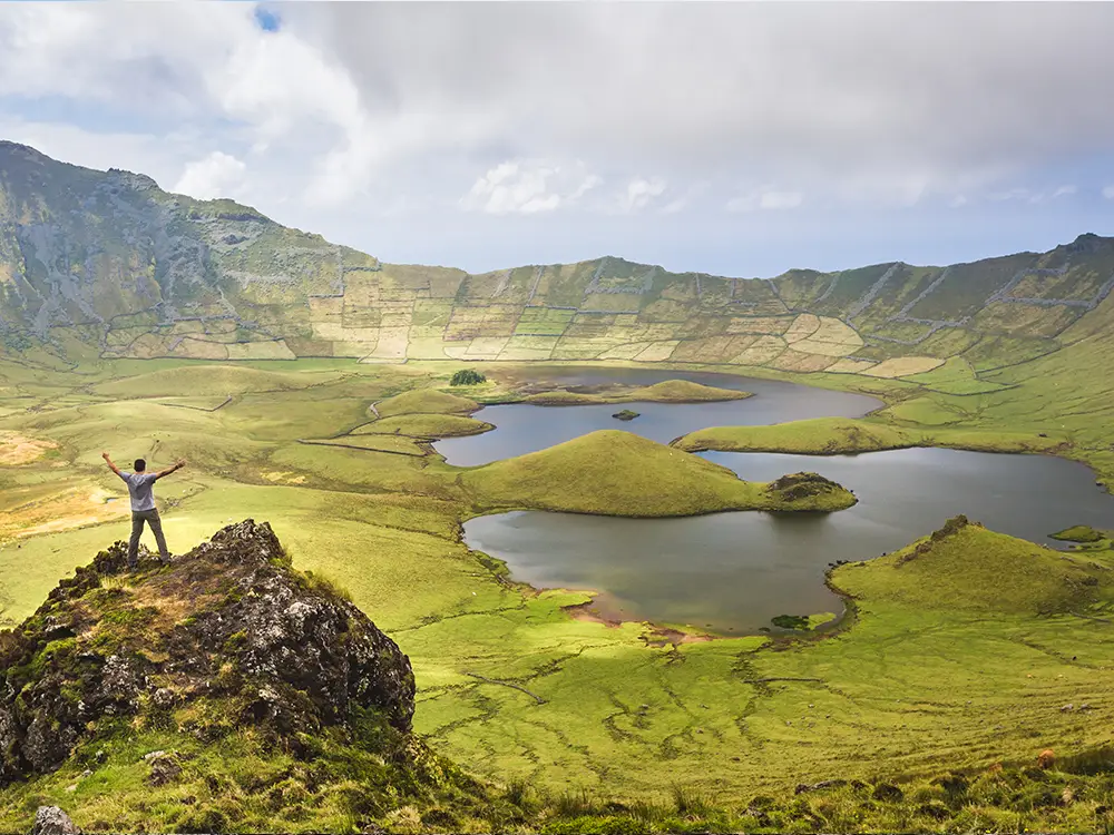 Individual standing on a rock with arms raised, overlooking Caldeirão on Corvo Island, Azores.