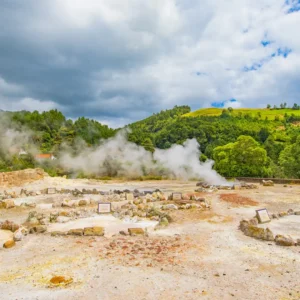 Geothermal area at Furnas Lake with steam rising from the ground and rock formations.