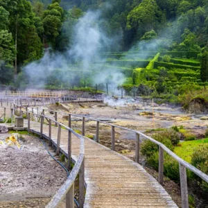 Wooden pathway winding through a geothermal area with steam rising from the ground at Furnas Lake.