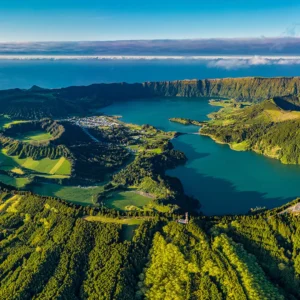 Aerial view of Sete Cidades, a volcanic crater lake in the Azores with green hills and blue water.