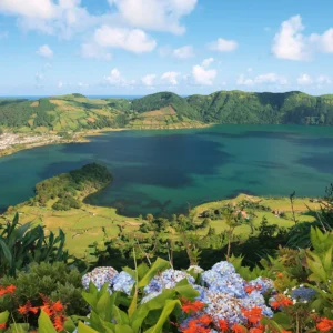 A panoramic view of Lagoa do Fogo, showcasing the blue water surrounded by green hills and flowers.