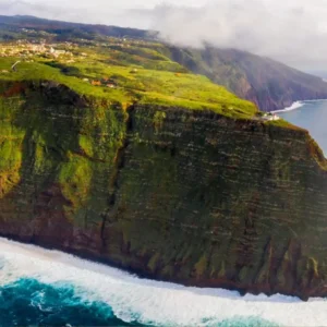 Aerial view of Ponta do Pargo cliffs with green vegetation and ocean waves below.