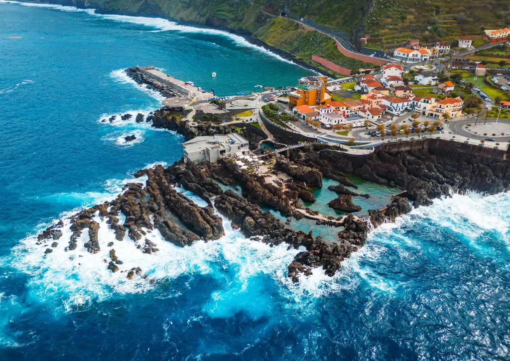 Aerial view of Porto Moniz with rocky coastline and ocean waves crashing against the shore.
