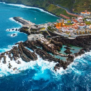 Aerial view of Porto Moniz with rocky coastline and ocean waves crashing against the shore.
