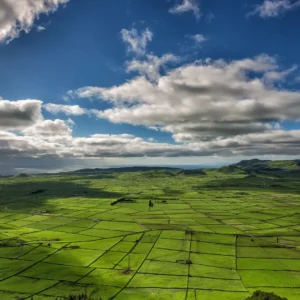 Expansive green landscape featuring fields and a cloudy sky over a hilly terrain.