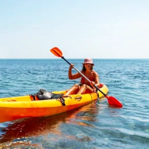 Individual paddling in an orange kayak on calm water under a clear sky.