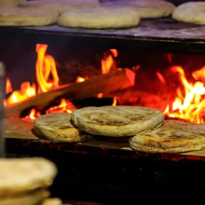 Flatbreads baking on a wooden surface above an open flame in a traditional setting.