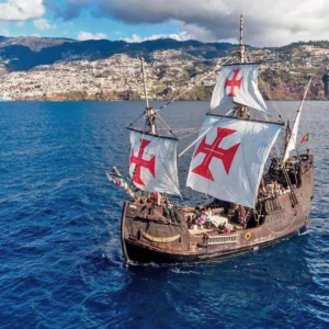 A replica of the Santa Maria ship sailing on the ocean with sails displaying red crosses.