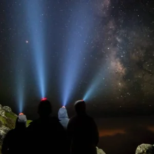 Silhouetted figures with headlamps illuminating the night sky filled with stars and the Milky Way.