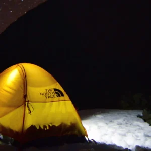 Yellow tent set up on a snowy surface under a starry night sky.