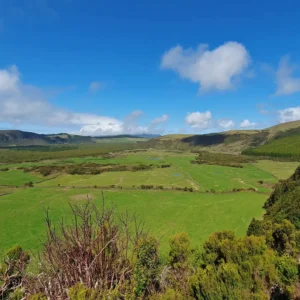 Expansive green landscape featuring rolling hills and a clear blue sky with scattered clouds.