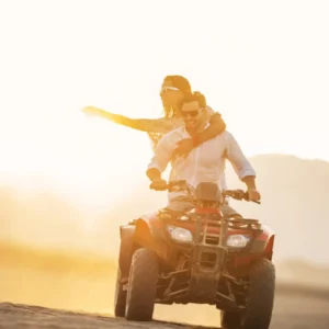 A man and woman riding an all-terrain vehicle during sunset, with the sun setting in the background.