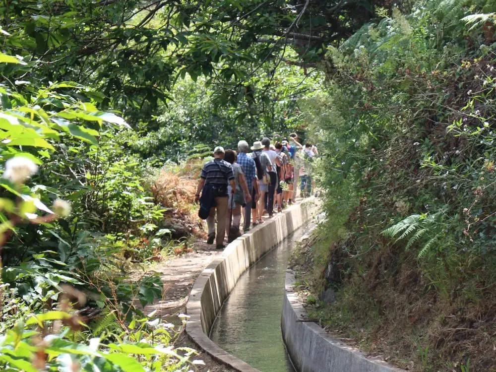 A group of hikers walking along a narrow water channel in Serra de Água