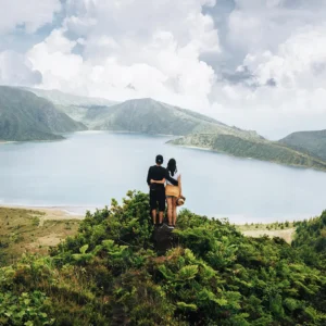 A couple standing on a hill overlooking a large lake surrounded by green hills in Sete Cidades.