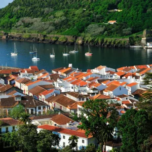 Aerial view of a coastal town on Terceira Island with red-roofed buildings and boats in the water.