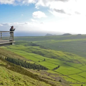 Person standing on a viewpoint overlooking green fields and hills on Terceira Island.