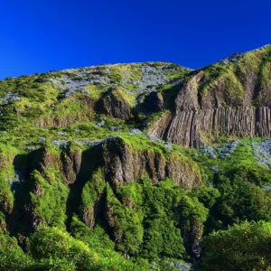 A mountain featuring prominent vertical rock formations and lush greenery on its slopes.