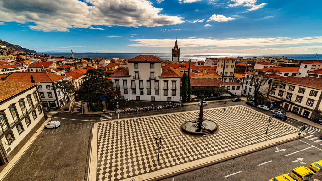 View of a historic square in Funchal, Madeira, featuring tiled patterns and surrounding buildings.